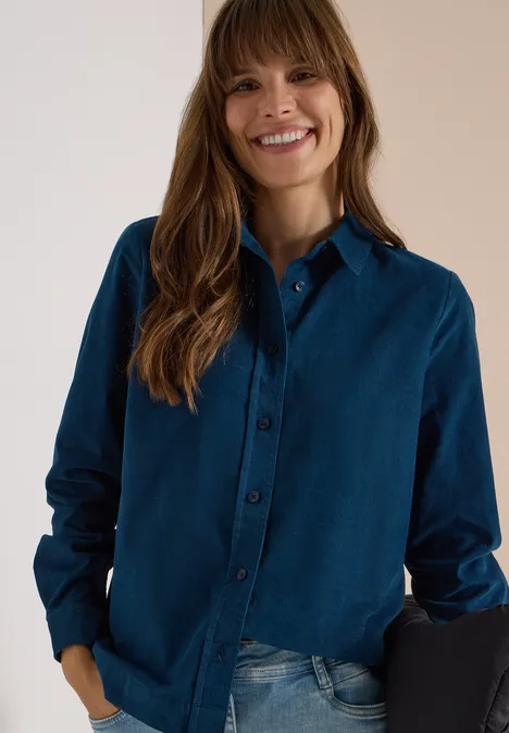 Chemisier à manches longues en velours côtelé moonlight blue Femme souriante aux cheveux bruns longs, portant une chemise bleu foncé et un jean.
