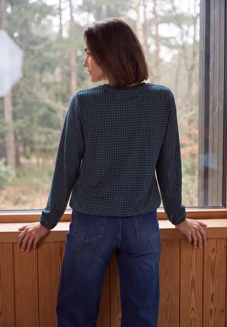 Langarm Bluse mit Rundhals und Print urban dark blue Frau lehnt sich im karierten Oberteil an Fensterrahmen und blickt auf Waldlandschaft.