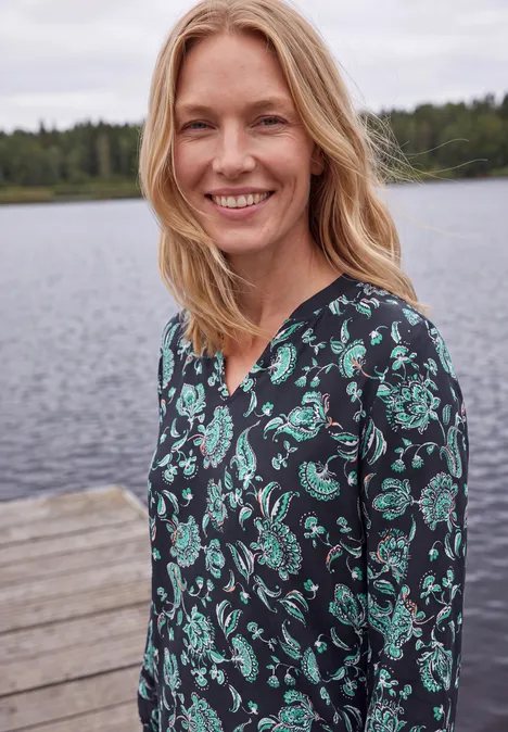 Chemisier à manches longues, à col fendu et imprimé urban dark blue Une femme souriante en robe à motifs pose au bord d’un lac.