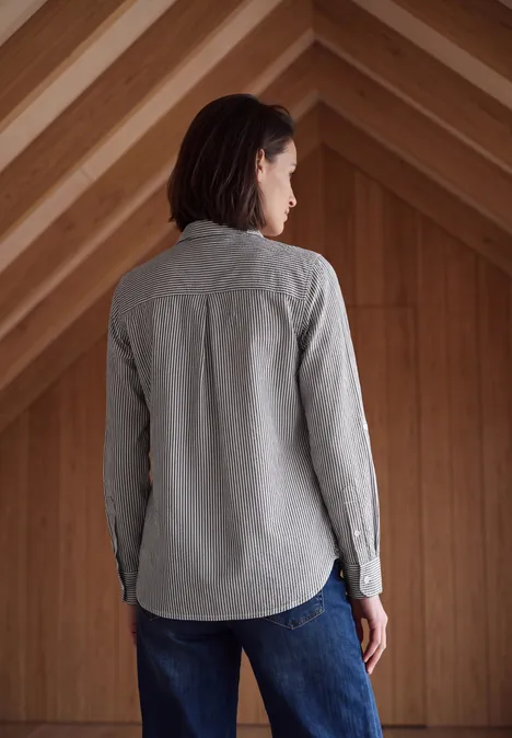 Femme vue de dos portant une chemise grise et un jean dans un espace en bois.