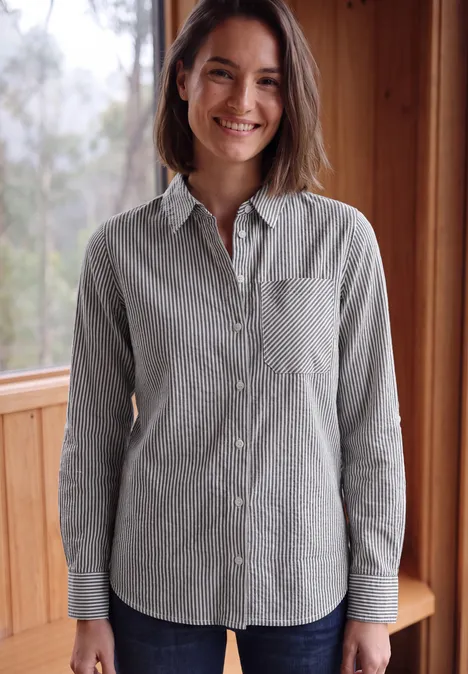 Femme souriante en chemise gris à fines rayures devant un mur en bois.