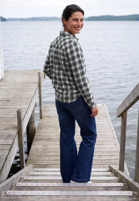 Langarm Flanell Bluse mit Karomuster vanilla white Eine Frau steht auf einem Steg am See, trägt karierte Bluse und Jeans und lächelt zurück zur Kamera.