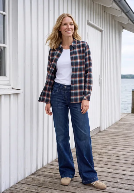 Chemisier en flanelle à manches longues et à carreaux urban dark blue Femme en chemise à carreaux et jean sur une jetée devant une maison en bois blanc au bord de l'eau.