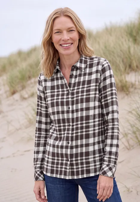 Frau mit kariertem Hemd lächelt am Strand vor Dünen.