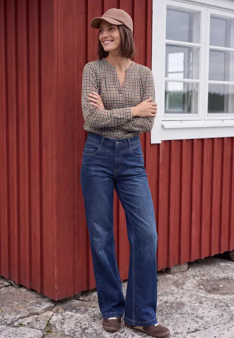 Langarm Tunika mit Split Neck und Print mocha brown Eine lächelnde Frau in Jeans, kariertem Hemd und Cap lehnt entspannt vor einem roten Holzhäuschen mit weißen Fenstern.