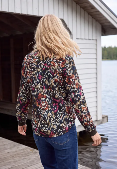 Une femme aux cheveux blonds, chemise colorée et jean, marche sur un ponton au bord du lac.