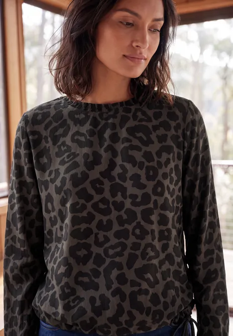 Langarm Blusenshirt mit Smokdetails truffle brown Frau trägt dunkelgrünen Pullover mit Leopardenmuster und steht neben einem Fenster.