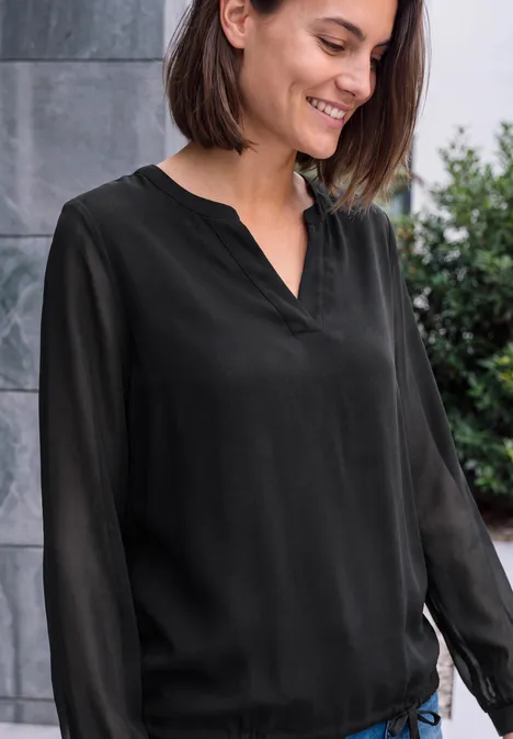 Langarm Bluse mit V-Neck und Strukturmix Black Lächelnde Frau mit schwarzer, langärmliger Bluse und dunklen Haaren steht vor einer grauen Wand im Freien.