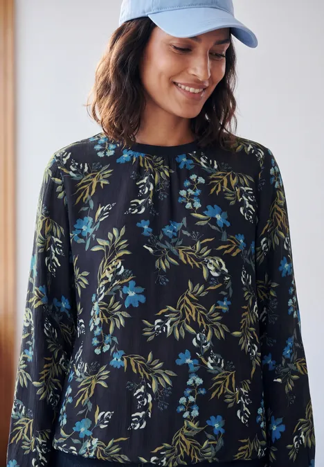 Crepe Bluse mit floralem Muster urban dark blue Eine Frau trägt eine blaue Kappe und ein schwarz-blau-grünes Blumenshirt