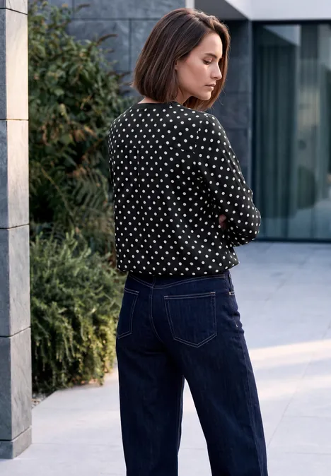 Crepe Bluse mit Punktemuster Black Eine Frau in gepunkteter Bluse und Jeans steht vor modernem Gebäude und blickt zur Seite.