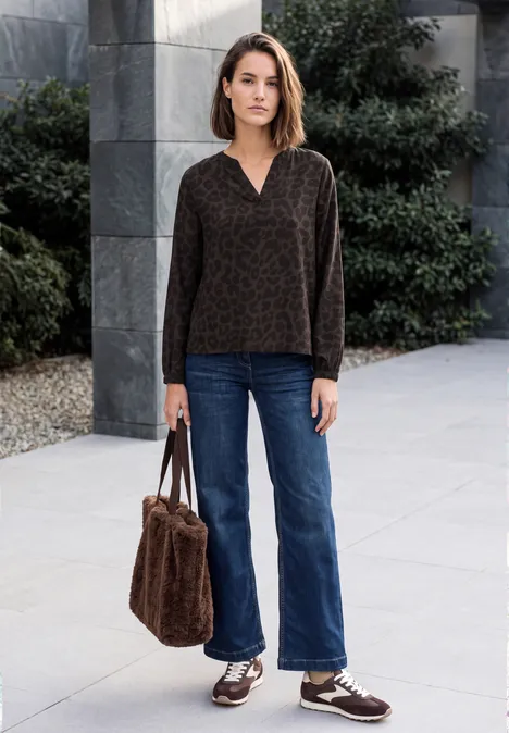 Frau steht Outdoor, trägt braunen gemusterten Pullover, weite Jeans, braune Schuhe und hält eine braune Fell-Tasche.