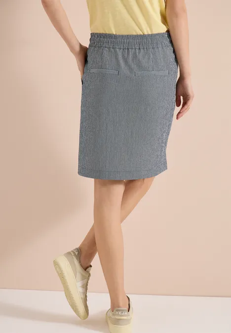 Frau trägt knielangen, gestreiften Rock mit elastischem Bund und Taschen, dazu gelbe Sneaker.