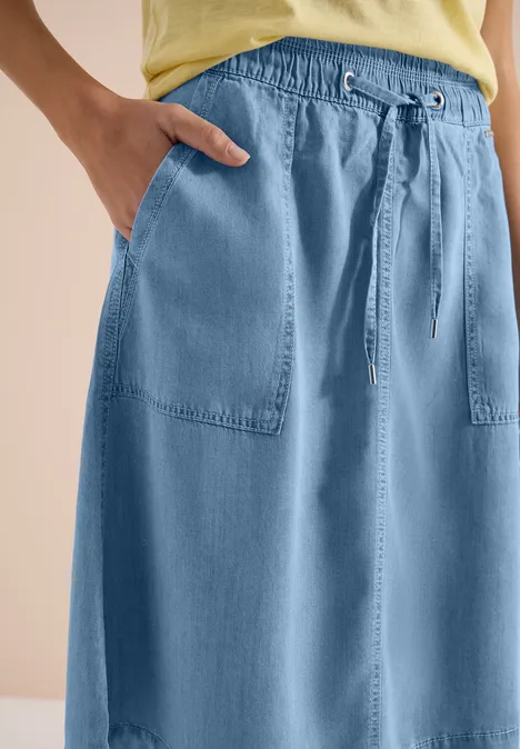 Hellblauer Jeansrock mit elastischem Bund, Tunnelzug und aufgesetzten Taschen, kombiniert mit gelbem Top.