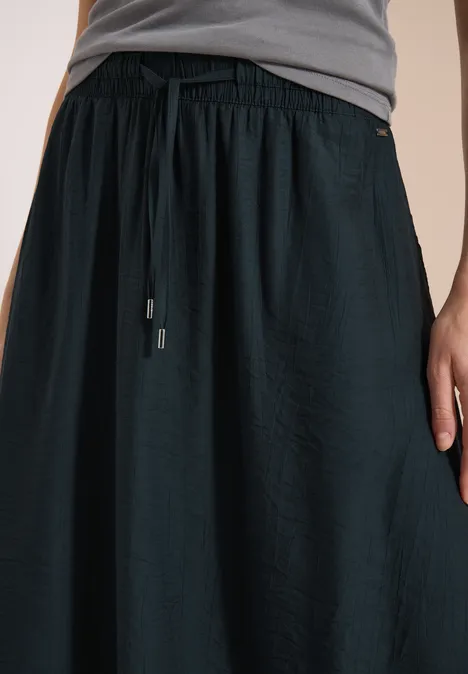 Persoon draagt een losse zwarte rok met trekkoord in de taille en een grijs t-shirt voor een lichte achtergrond.