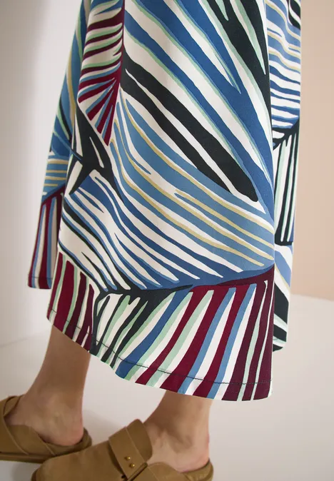 Person trägt langes, bunt gestreiftes Kleid mit diagonalen und horizontalen Mustern in Blau, Grün, Rot und Weiß.