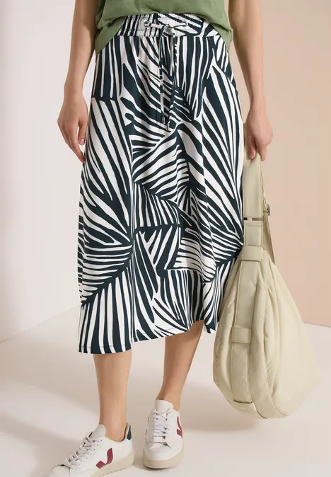 Midirok met zwart-wit bladpatroon, witte sneakers, groen topje en ecru tas.