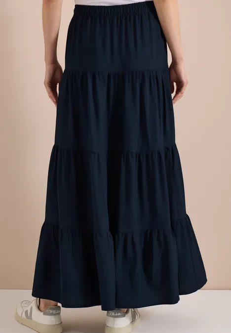 Vue de dos d'une jupe longue bleue marine à volants, taille élastique, portée avec des baskets blanches.