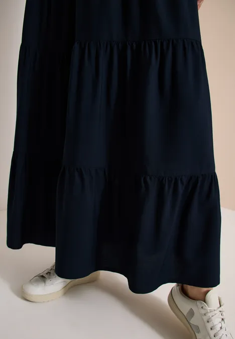 Bas du corps: robe longue noire à volants et baskets blanches.