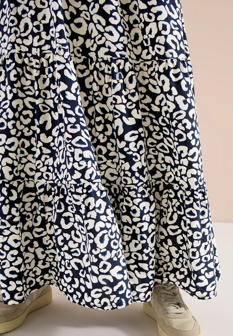 Weit schwingender Rock mit weißem Leopardenmuster auf dunkelblauem Stoff und hellen Sneakern.