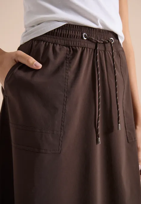 Donkerbruine, losse rok met elastische taille, koordsluiting en zijzak, gecombineerd met wit topje.