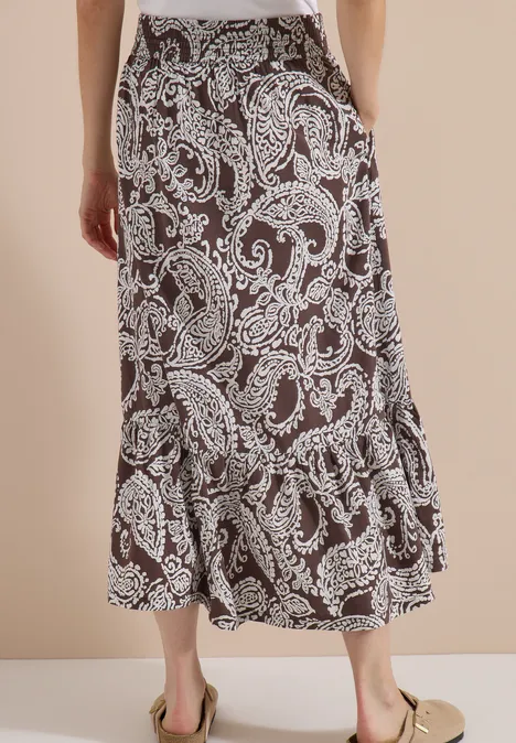 Raffinierter schwarzer Midirock mit weißem Paisley-Muster und Volant am Saum, getragen mit beigen Mules.