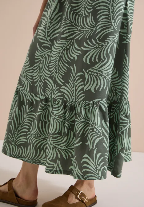 Langes, grün gemustertes Stufenkleid im Blättermuster und braune Sandalen mit Schnalle.