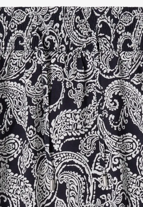 Schwarzer Stoff mit weißem Paisley-Muster, geschwungene Ornamente und Blüten.