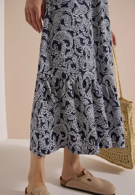 Femininer Look mit gemusterter Midirock, Basttasche und stylischen beigen Mules.