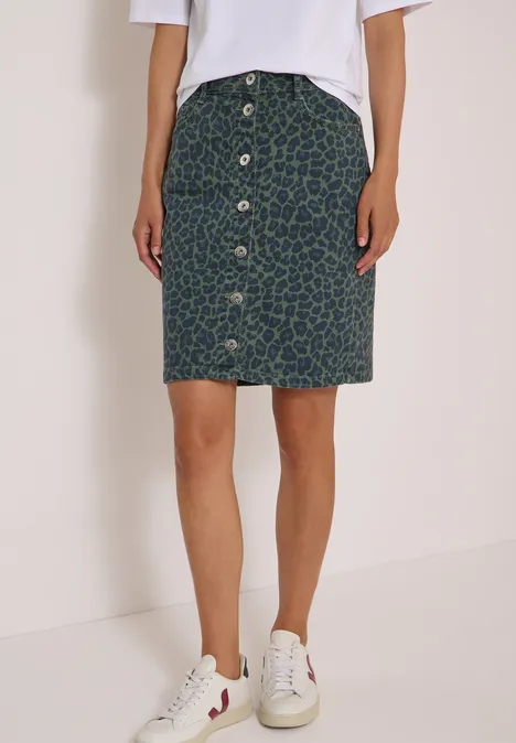 Kniehoge denimrok met luipaardprint dried olive green Persoon draagt wit T-shirt, groene knielange rok met luipaardprint en knopen voorop, witte sneakers.