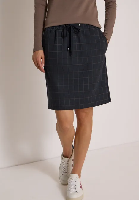 Knielanger Rock mit Tapedetails urban dark blue Frau in einem knielangen, karierten Rock mit Kordelzug, beigem Langarmshirt und weißen Sneakern.