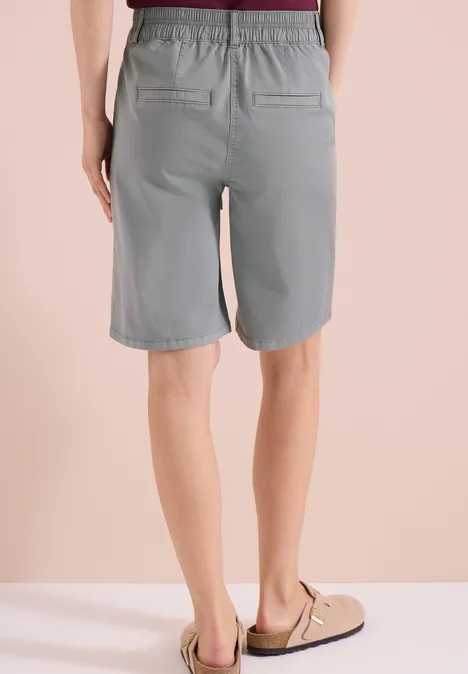 Achteraanzicht van een persoon in grijze bermudashorts en sandalen voor een beige achtergrond.