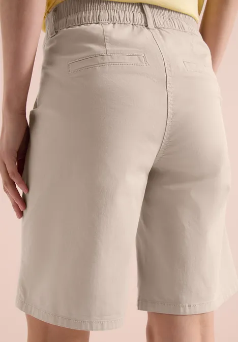 Persoon van achteren in beige knielange short met elastische tailleband en achterzakken.