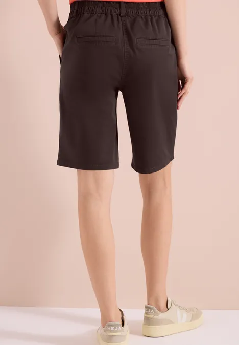 Achteraanzicht van iemand in zwarte knielange shorts met beige sneakers voor een lichte achtergrond.