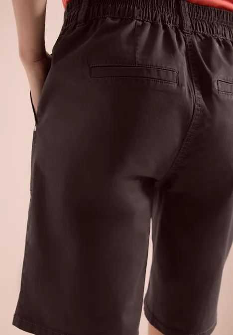 Achteraanzicht van een persoon in donkere, knielange short met achterzakken.