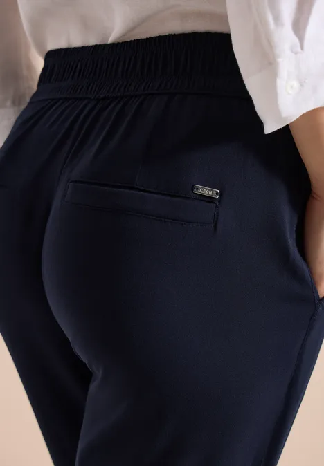 Seitliche Ansicht einer Person in dunkelblauen, elastischen Hosen mit Gesäßtasche und lockerem Oberteil.