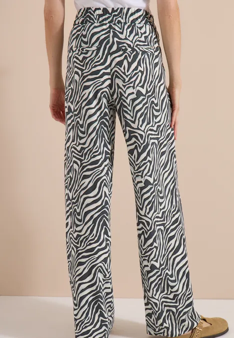 Pantalon Straight Leg avec imprimé zèbre palm breeze green Femme de dos portant un pantalon large à imprimé zèbre noir et blanc sur fond beige.