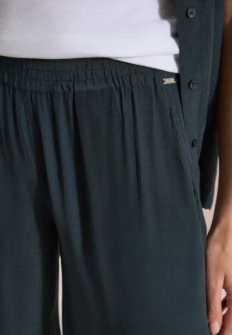 Detail: loszittende donkergroene broek met elastische taille, wit topje en donkergroene jas.