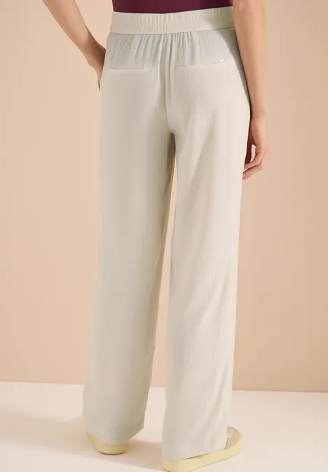 Pantalon féminin ample beige avec taille élastique et poches plaquées à l’arrière.