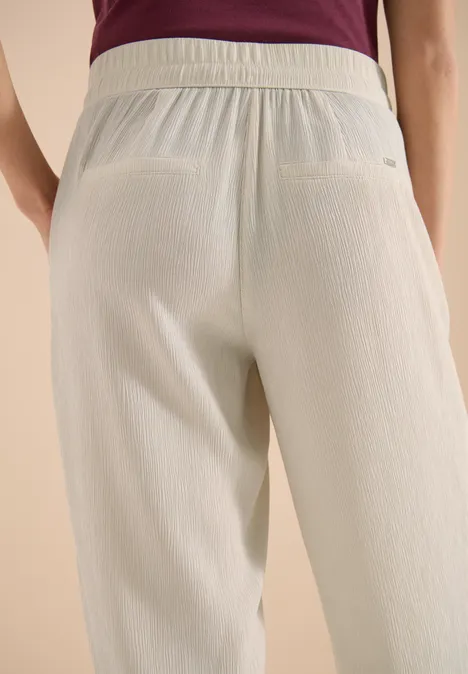 Vue arrière d'une personne portant un pantalon clair texturé et un haut violet.