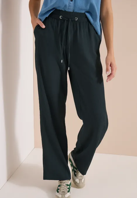 Schwarze, weite Hose mit Kordelzug in der Taille, kombiniert mit weißen Sneakern und blauem Oberteil.