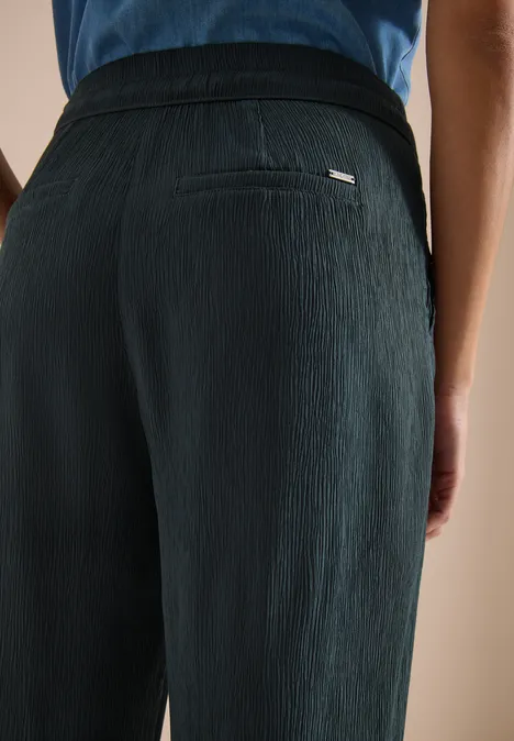 Person trägt schwarze, strukturierte Hose, Rückenansicht.