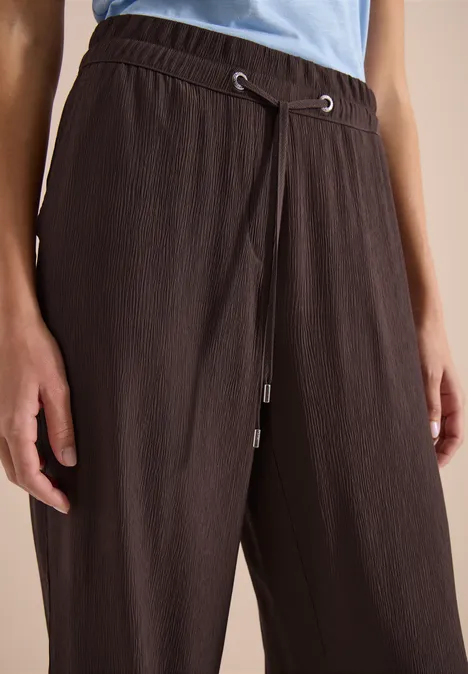 Nahaufnahme einer Person in braunen, strukturierten Hose mit Kordelzug und hellblauem Oberteil.