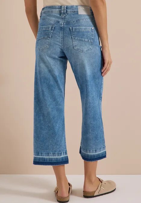 Rückansicht: Person in weiten, knöchellangen Jeans und beigen Loafern.