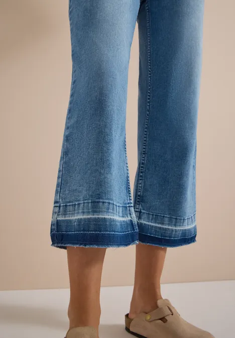 Frau trägt weite blaue Jeans-Culottes mit Ziernähten und beigefarbenen Mules mit Schnalle.