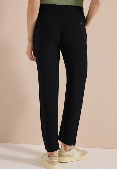 Iemand draagt een zwarte broek en lichte sneakers voor een neutrale, lichte achtergrond.