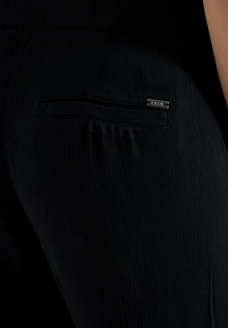 Close-up van persoon in zwarte, gestructureerde broek met klein ritssluitingzakje op het achterwerk.