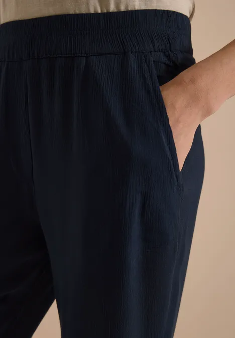 Donkerblauwe, losse broek met elastische taille en zijzak, hand in de zak.