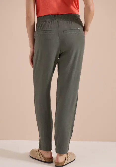Achteraanzicht van een persoon met losse olijfgroene broek met elastische taille en sandalen.