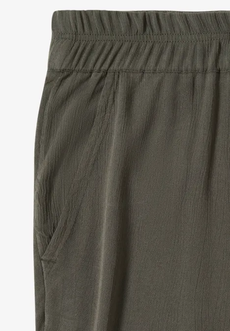 Close-up van een olijfgroene stofbroek met elastische tailleband en zijzak.