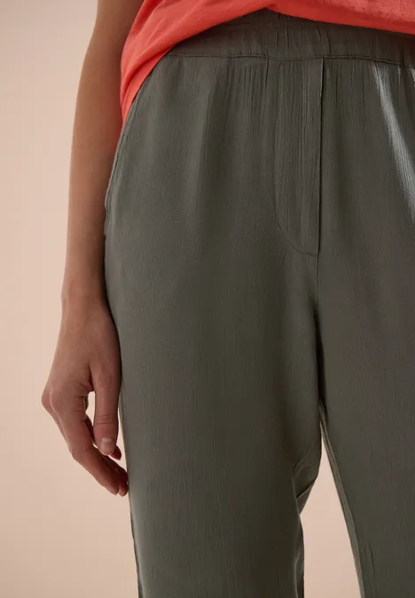 Close-up van een persoon in een loszittende groene broek en een rood topje.